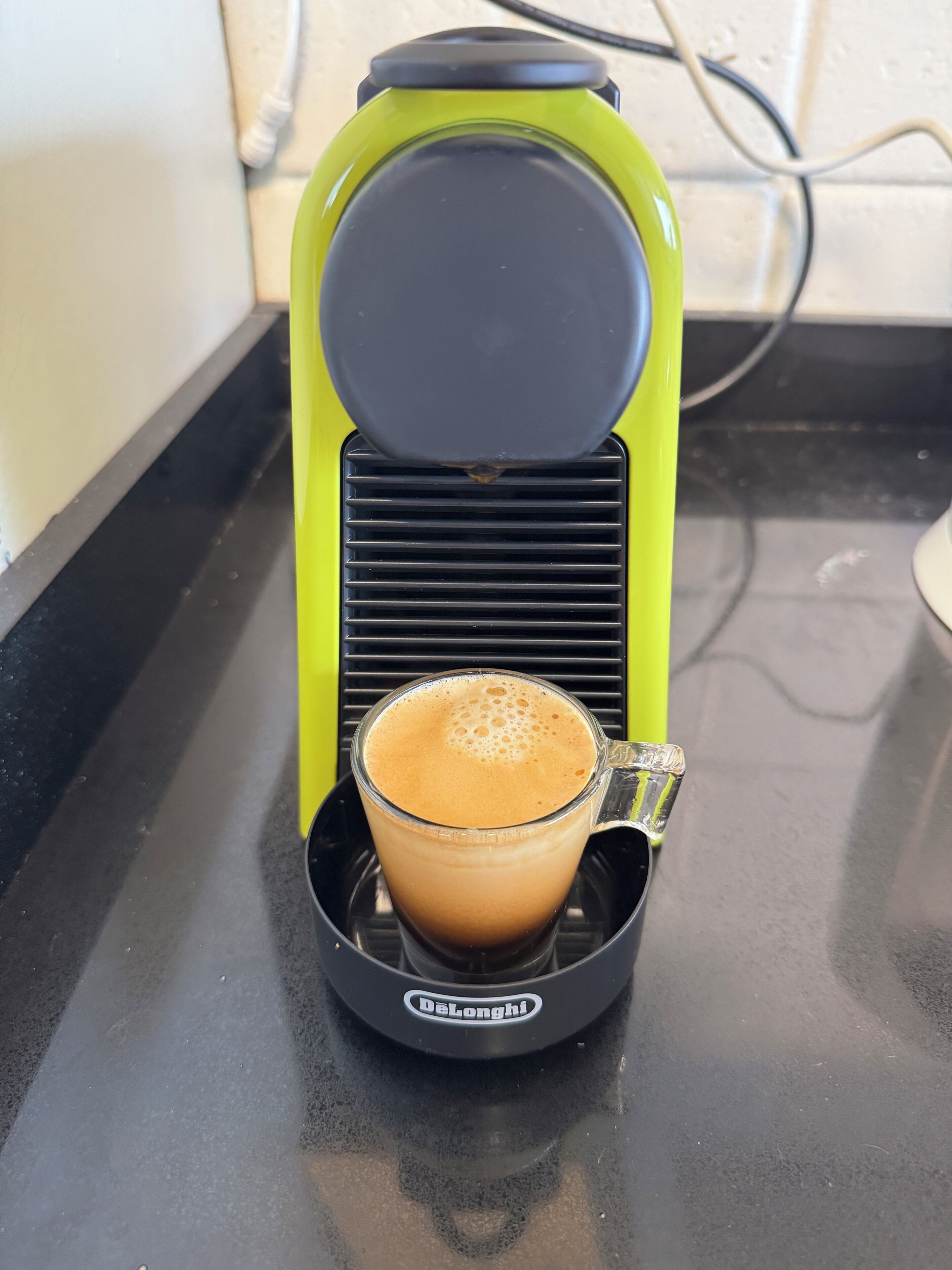 A coffee maker with a glass cup on a black countertop.