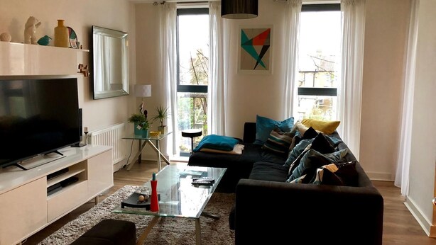 Una sala de estar moderna con un televisor de pantalla plana, una mesa de centro de vidrio, un sofá y un ventanal con cortinas.
