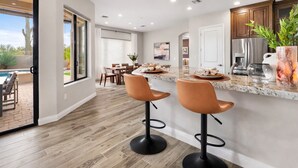 Een moderne keuken met een marmeren aanrecht, twee barkrukken en een eethoek met een tafel en stoelen.