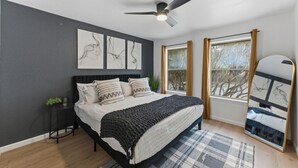Une chambre à coucher avec un lit, un ventilateur de plafond, une fenêtre avec des rideaux et des œuvres d’art accrochées au mur.