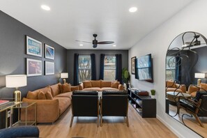 A modern living room with a sofa, a coffee table, a TV, and a ceiling fan. - Spacious Retreat Near Downtown (Austin)