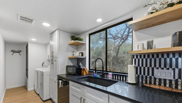 Une cuisine moderne avec des meubles blancs, un plan de travail noir et une fenêtre donnant sur des arbres.