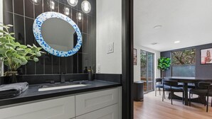Une salle de bain moderne aux couleurs noir et blanc, avec un miroir rond orné d’un motif bleu et blanc, et une plante en pot.