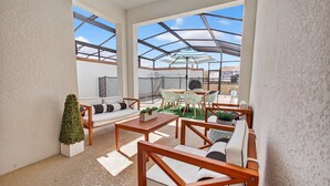 Eine überdachte Terrasse im Freien mit Tisch und Stühlen, einer Couch und einem kleinen Topfpflanzen.