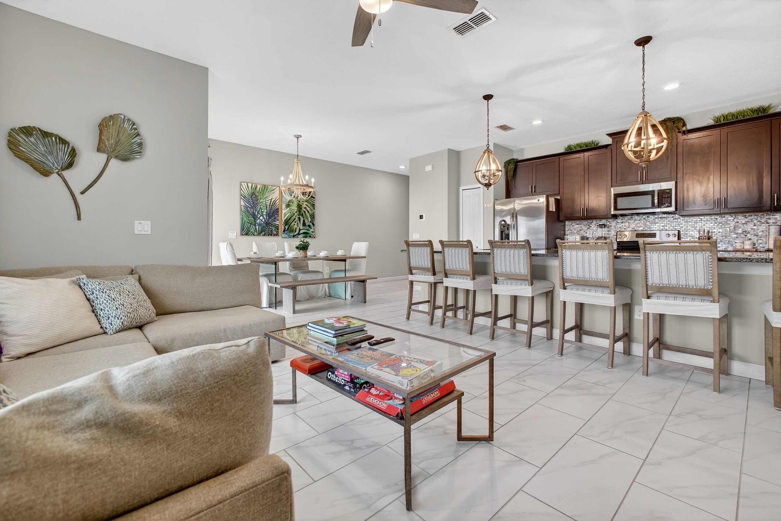 A modern living room with a glass coffee table, a sofa, and a dining area with chairs and a chandelier.