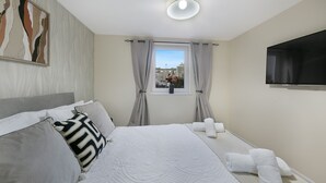 Habitación de hotel con cama, televisión de pantalla plana, ventana con cortinas y un cuadro en la pared.