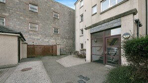 Un edificio con fachada de piedra, entrada protegida por una reja y acceso a nivel de calle con puerta de cristal.