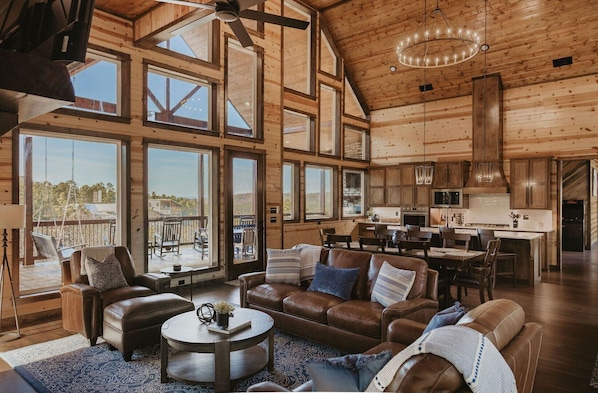 A spacious living room with a large brown leather sofa, a coffee table, and a view of the outdoors through large windows. - Heated Outdoor Pool, Video Games, Play-Set, Air Hockey, Rocky Waters (Broken Bow)