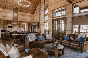 Ein geräumiges Blockhaus-Interieur mit Essbereich, Küche und Wohnzimmer, möbliert mit Ledersofas und einem Couchtisch.