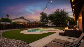 A backyard with a swimming pool, outdoor seating, string lights, and a wooden fence. - Nectar Nest, Video Tour, Pool, Spa, Fire Pit Arcade Game Room, King Master Suite (Hemet)