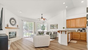 A spacious living area with a fireplace, a ceiling fan, and a kitchen with wooden cabinets. - Nectar Nest, Video Tour, Pool, Spa, Fire Pit Arcade Game Room, King Master Suite (Hemet)