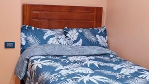 A bedroom with a wooden headboard, a bed with a blue floral bedspread, and a grey throw blanket. - Cusco Apartment, Prime Location (Cusco)