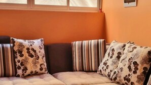 A sectional sofa with floral cushions, a glass coffee table, and a window with blinds. - Cusco Apartment, Prime Location (Cusco)