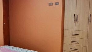 A bedroom with a bed covered in a floral-patterned bedspread, a wardrobe with multiple drawers, and two electrical outlets on the wall. - Cusco Apartment, Prime Location (Cusco)