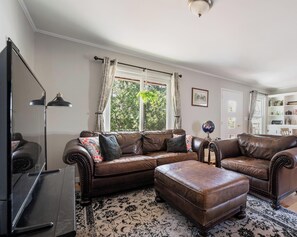 Ein Wohnzimmer mit einem braunen Ledersofa, einem passenden Hocker, einer großen Stehlampe und einem gemusterten Teppich.