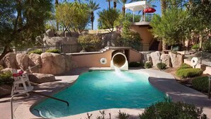 A swimming pool with a water slide, surrounded by rocks and palm trees. - COACHELLA LODGING!
Shuttle to Coachella next door, easy there and back! (Rancho Mirage)