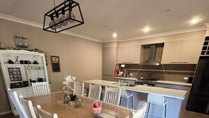 A modern kitchen with white cabinets, a central island, and a dining area with a wooden table and white chairs.