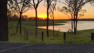 A rural landscape with trees, a road, and a body of water during sunset.