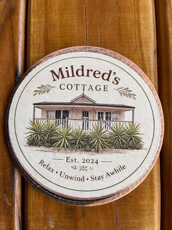 A circular wooden plaque with the text 'Mildred's Cottage' and 'Est. 2024' along with a house illustration and the phrase 'Relax. Unwind. Stay Awhile.' - Country Escape for Every Occasion – Relax, Unwind & Discover the BVRT (Coominya)