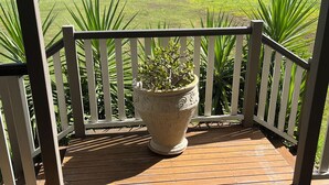 A wooden deck with a white railing, a large decorative planter, and a view of a grassy field and trees in the background.