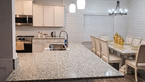 Una cocina moderna con encimeras de granito, electrodomésticos de acero inoxidable y un comedor con una mesa de mármol y detalles dorados.