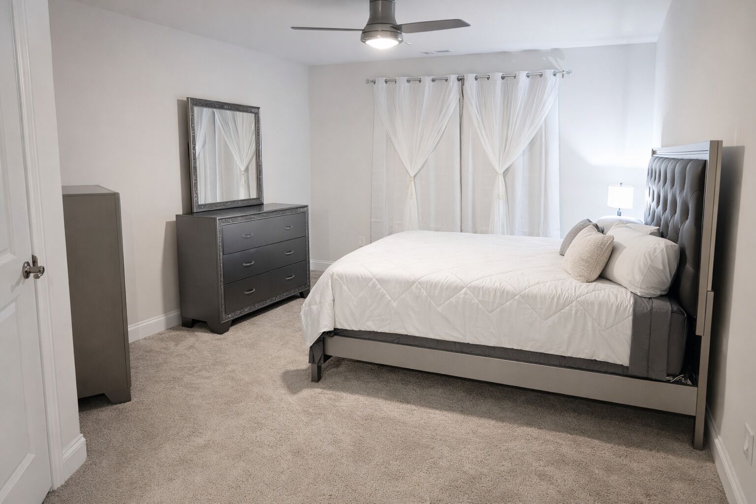 A bedroom with a bed, a dresser, a mirror, and a ceiling fan.