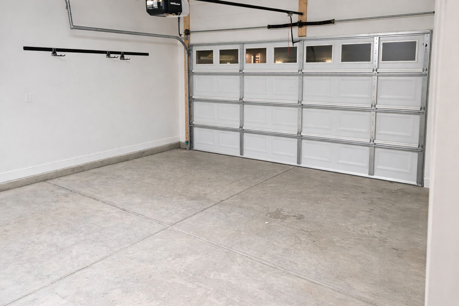 Een garage met een betonnen vloer, een witte garage deur en een lamp aan het plafond.