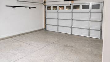 Een garage met een betonnen vloer, een witte garage deur en een lamp aan het plafond.