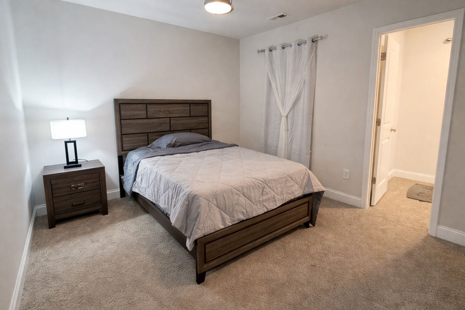 Un dormitorio con cama, mesita de noche, lámpara y una puerta.