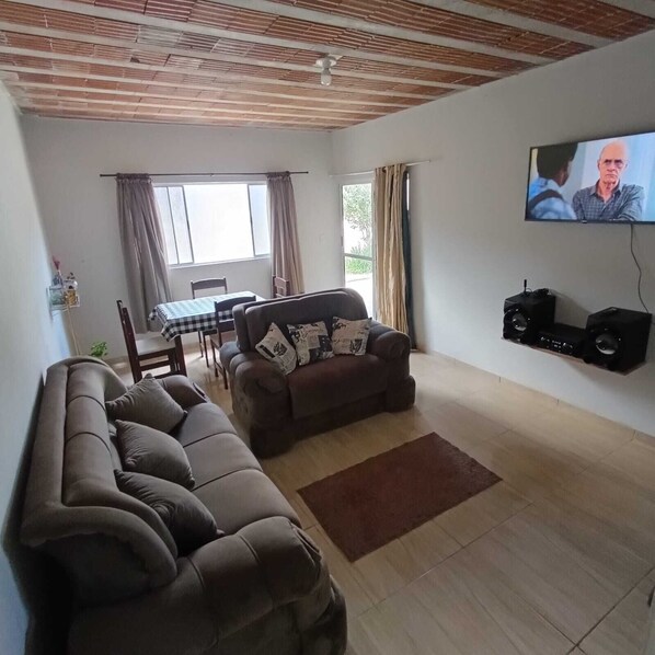Ein Wohnzimmer mit einer Couch, einem an der Wand montierten Fernseher und einem Essbereich mit Tisch und Stühlen.
