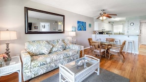 A living room with a sofa, coffee table, and dining area with chairs. - Seawinds 702 (North Myrtle Beach)