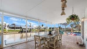 A covered patio with a table and chairs, a hanging plant, a pool, and a view of the surrounding area. - Merritt Island Waterfront Oasis W/ Private Pool, Spa-like Hot Tub & Boating Dock! 🌅 (Merritt Island)