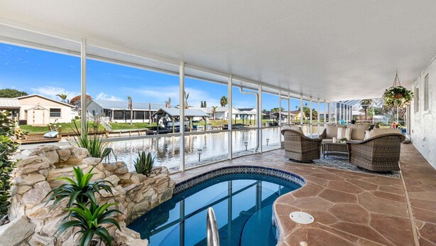 An indoor swimming pool with a stone floor, wicker furniture, and a view of the surrounding neighborhood. - Merritt Island Waterfront Oasis W/ Private Pool, Spa-like Hot Tub & Boating Dock! 🌅 (Merritt Island)