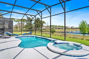 Un espace piscine doté d’un jacuzzi, de chaises longues et offrant une vue sur un lac et des maisons.