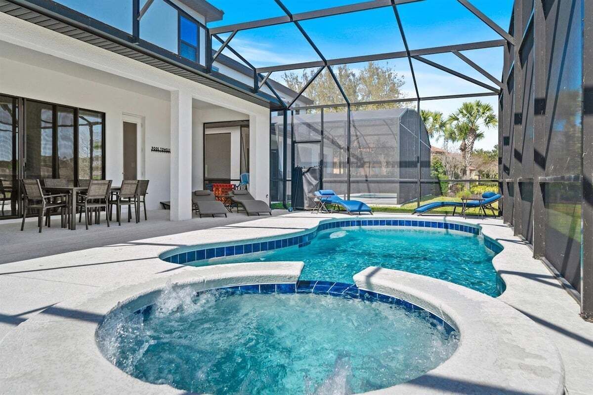 A modern outdoor pool area with a hot tub, lounge chairs, and a covered patio.