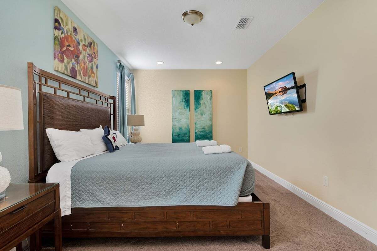 Une chambre à coucher bien rangée, avec un lit en bois, une table de chevet, une lampe et deux tableaux accrochés au mur.