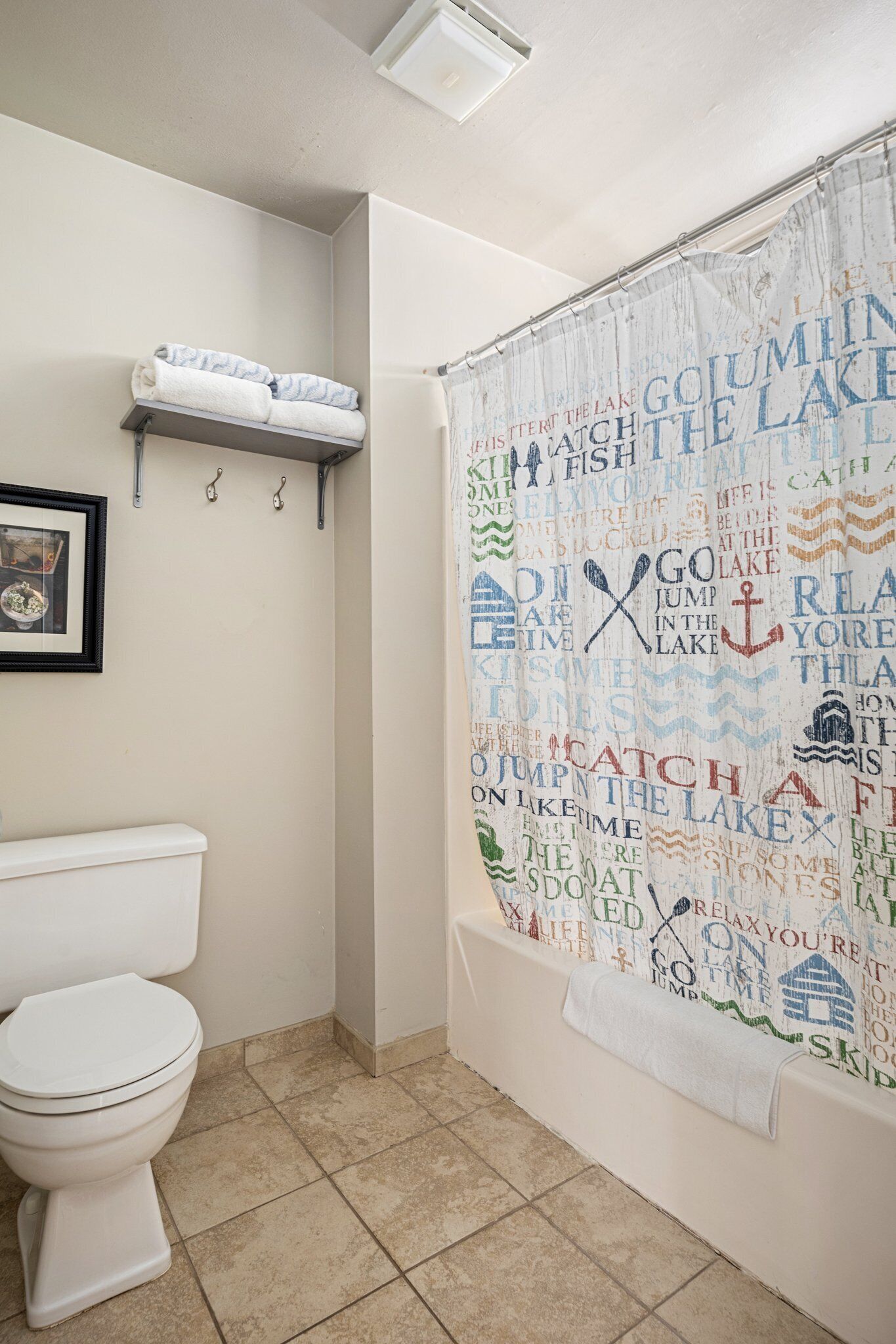 A bathroom with a white toilet, a towel rack with folded towels, and a shower curtain with text and graphics.