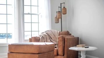 Ein gemütliches Wohnzimmer mit einem braunen Ledersofa, einem passenden Hocker und einem kleinen weißen Tisch.