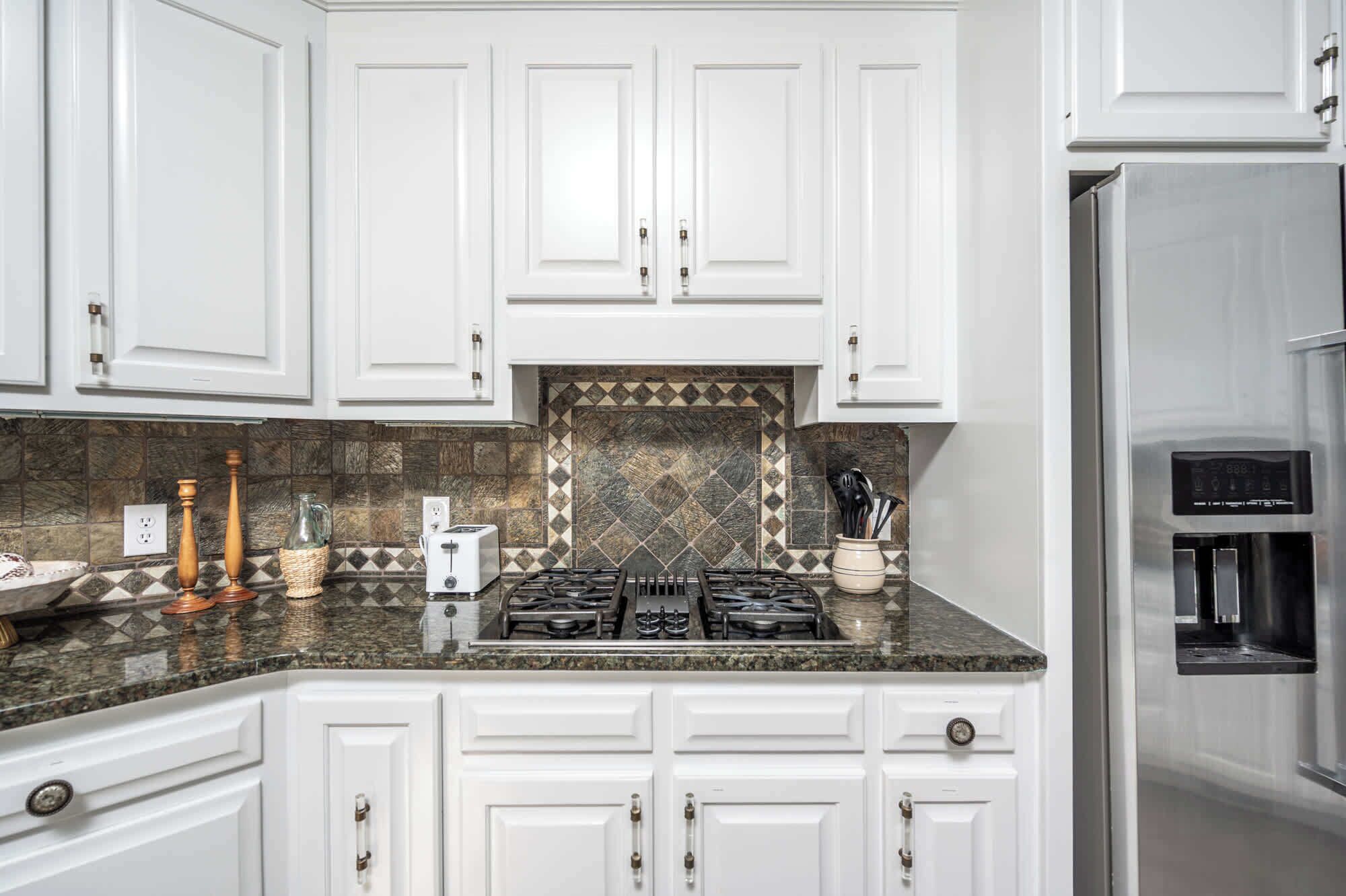 Una cocina con alacenas blancas, estufa a gas, tostadora y refrigerador de acero inoxidable.