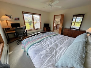 Een slaapkamer met een bed, bureau, stoel en een groot raam met uitzicht op een berg.