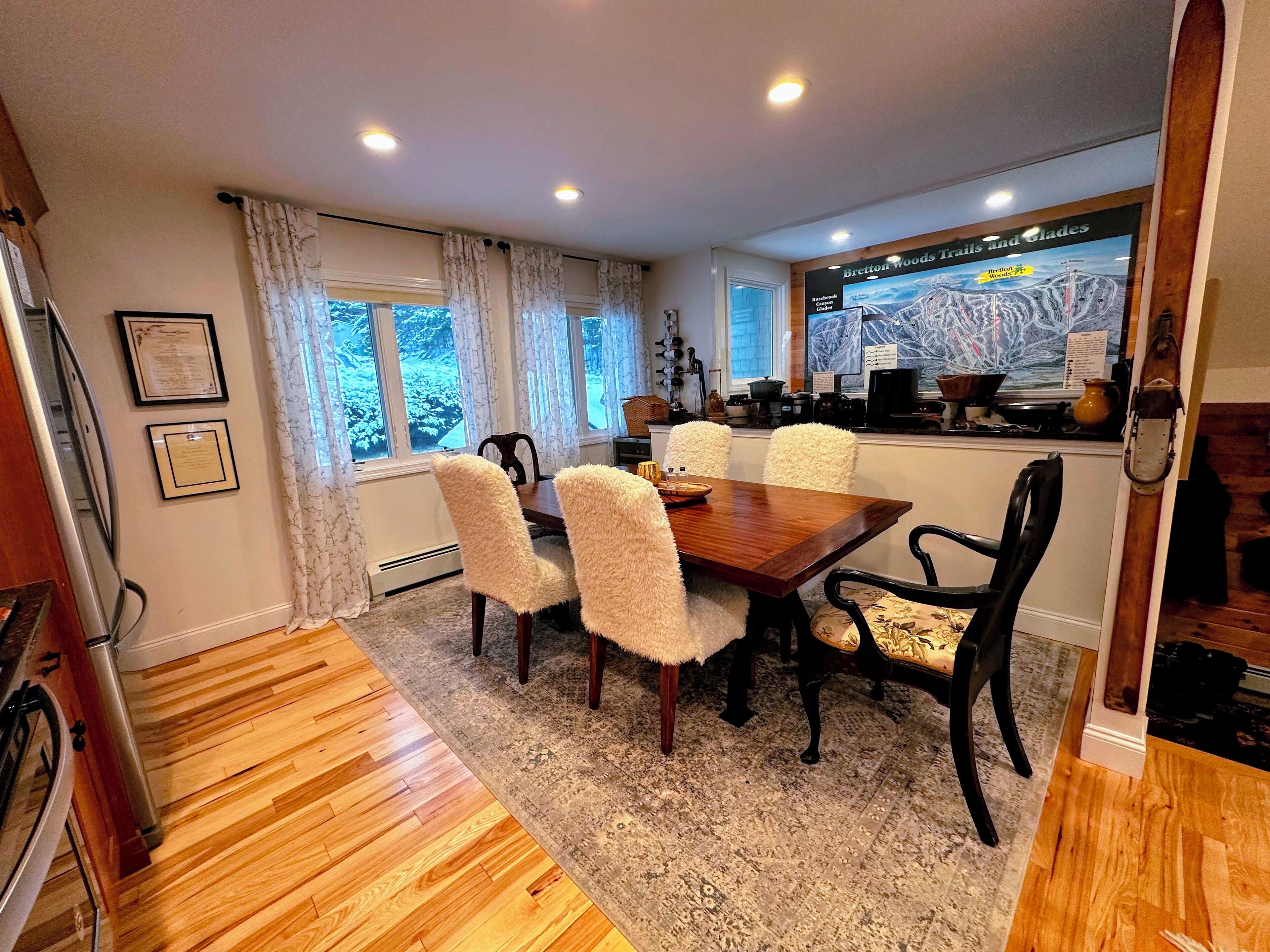 A dining area with a wooden table and chairs, a rug, and a window with curtains.