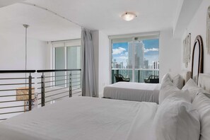 A modern hotel room with a large bed, a balcony with a railing, and a city view through large windows. - Brickell River Views- Modern Amenities in the City (Miami)