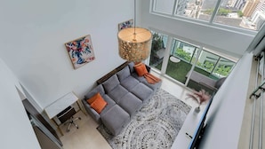 Un salon moderne avec un canapé d’angle gris, un tapis à motifs et une lampe suspendue.