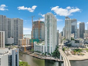 A high-rise building with a construction crane, surrounded by other tall buildings and a waterfront. - Brickell River Views- Modern Amenities in the City (Miami)