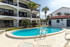 A swimming pool surrounded by a white building with balconies, a no swimming sign, and a small building with a red roof.