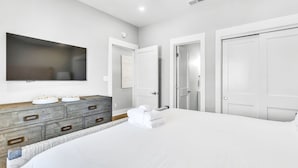A modern bedroom with a large bed, a wooden dresser, a flat-screen TV, and white doors.