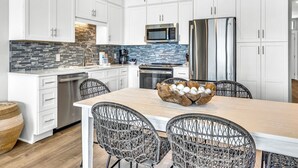 A modern kitchen with white cabinets, a stainless steel refrigerator, a microwave, and a tiled backsplash.