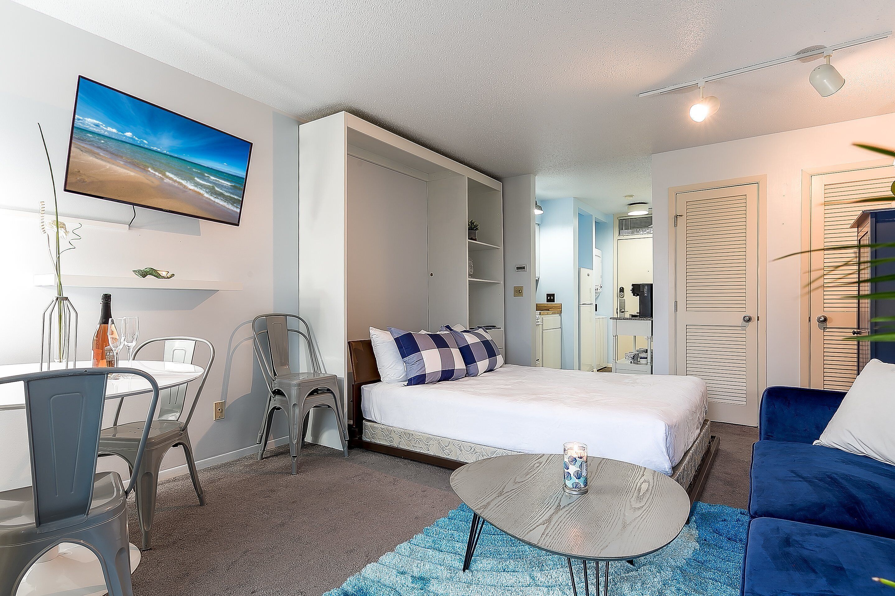 Ein Hotelzimmer mit einem Bett, einem Schreibtisch mit Stühlen, einem an der Wand befestigten Fernseher und einem blauen Sofa.