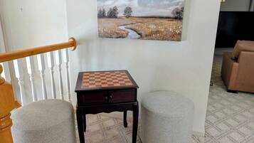 A chessboard on a table with two ottomans, a painting of a landscape, and a staircase.