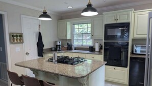 A kitchen with a central island, bar stools, a microwave, oven, and a coffee maker. - Lake Days Getaway - Lakeside Family Escape Near Hillsborough (Hillsborough)